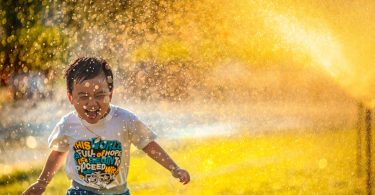 a young boy running through a sprinkle of water