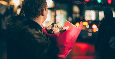 man in black faux fur coat holding bouquet of floweers