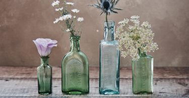 three green and one blue glass vases with flowers inside