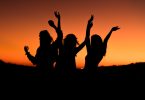 silhouette of three woman with hands on the air while dancing during sunset