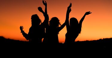 silhouette of three woman with hands on the air while dancing during sunset